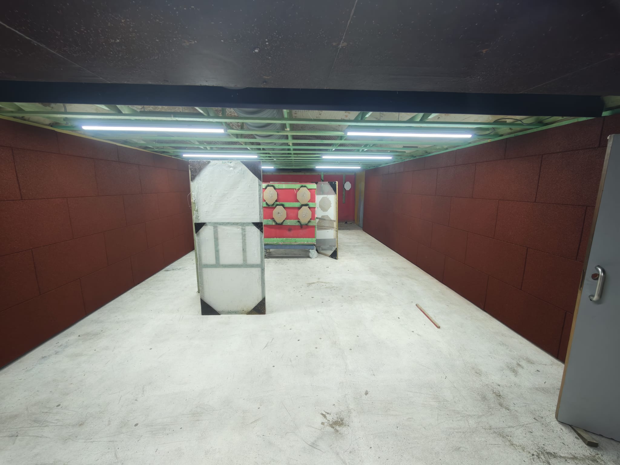 Een van de IPSC-parcoursstanden: bredere ruimte met rode rubberen wanden, papieren doelen, bewegende doelen en hindernissen opgesteld op de vloer.