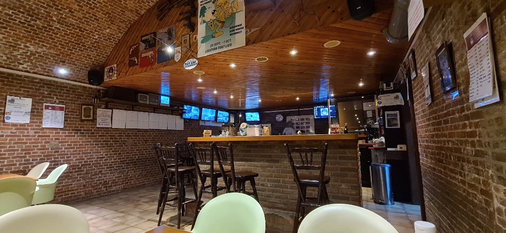 De kantine van Fort Lier — een bakstenen ruimte met houten gewelfplafond, een bar met barkrukken en wedstrijduitslagen aan de muur.