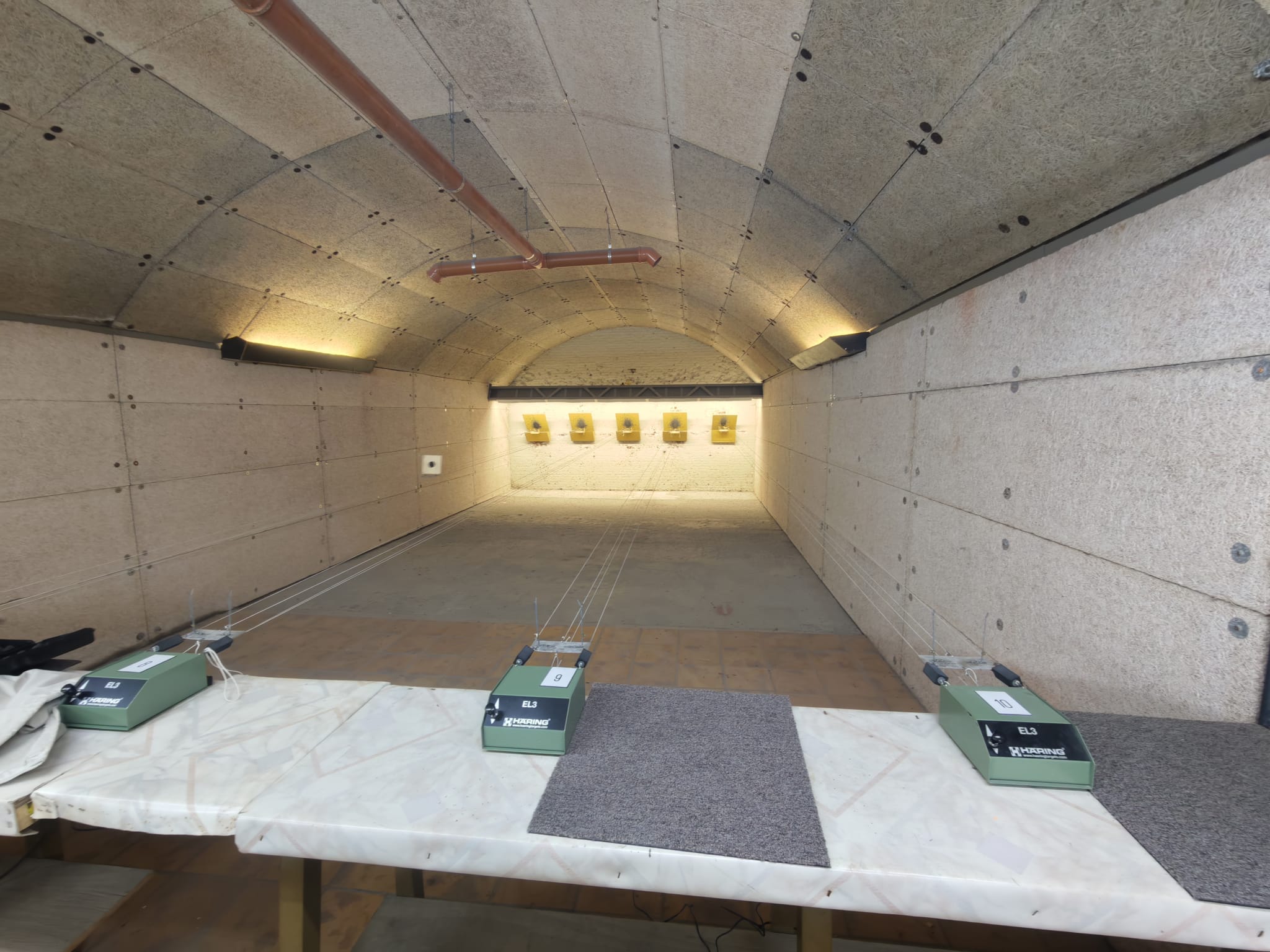 De luchtdrukstand van Fort Lier — gewelfde, met houtwol beklede banen met vijf gele doelen op de achtermuur en Häring EL3 elektronische scoringsunits op de schietbank.
